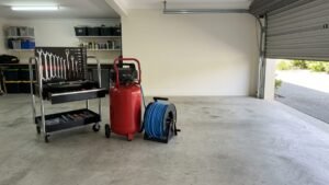 Portable air compressor on a garage floor beside a coiled hose