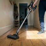 Cordless stick vacuum being pushed along hallway floorboards