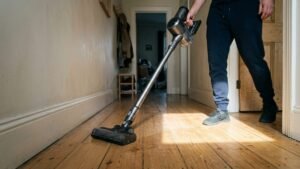 Cordless stick vacuum being pushed along hallway floorboards