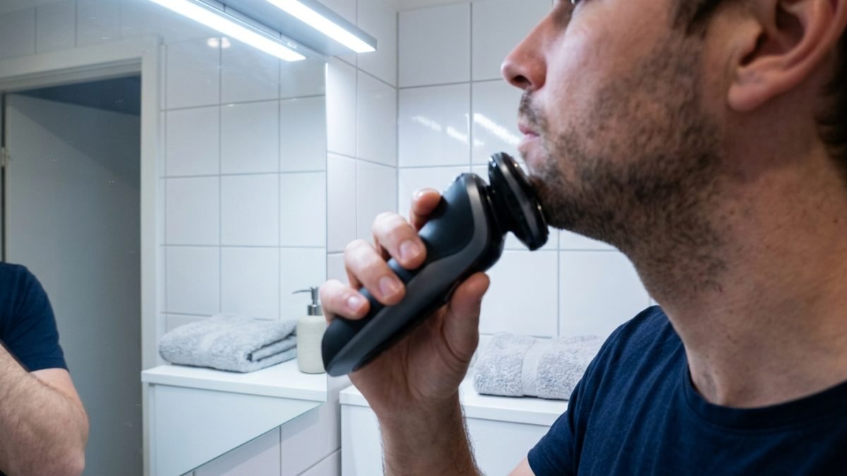 Man shaving with a cordless electric shaver in a home bathroom