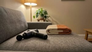 Handheld percussion massager resting on a couch cushion