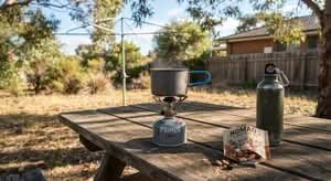 A person's hand holding the best camping stove in Australia on a picnic table, ready for outdoor cooking.