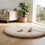A neutral cushioned baby play mat laid out on a wooden floor in a bright Australian home living room.