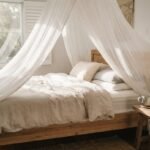 A dreamy sheer white bed canopy hanging over a cozy made bed in a sunlit Australian bedroom.