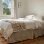 A neatly made bed with a neutral linen bed skirt in a sunlit Australian bedroom.
